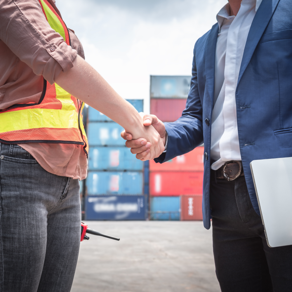 Two freight industry professionals shaking hands at a shipping yard, symbolizing partnership and trust in global logistics.